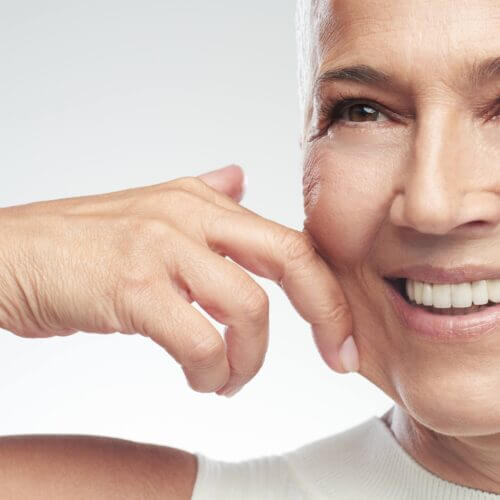 Gorgeous smiling Caucasian senior woman with short gray hair pinching her cheek. Beauty photography.